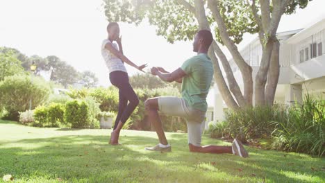 happy african american couple in sunny garden man kneeling holding ring proposing to woman
