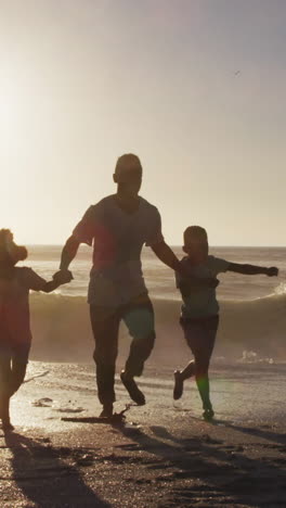 smiling african american family running and holding hands on sunny beach