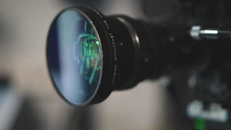 close up shot of professional camera lens reflecting green and blue studio lights with intricate glass elements, showcasing focus rings and internal optics for filmmaking and broadcast production