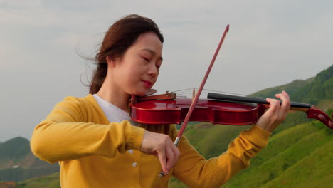 female musician plays the violin on the top of a mountain in asia