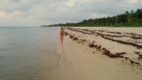 Aerial-tracking-shot-of-a-young-woman-in-a-bikini-running-along-the-beach-at-Cozumel