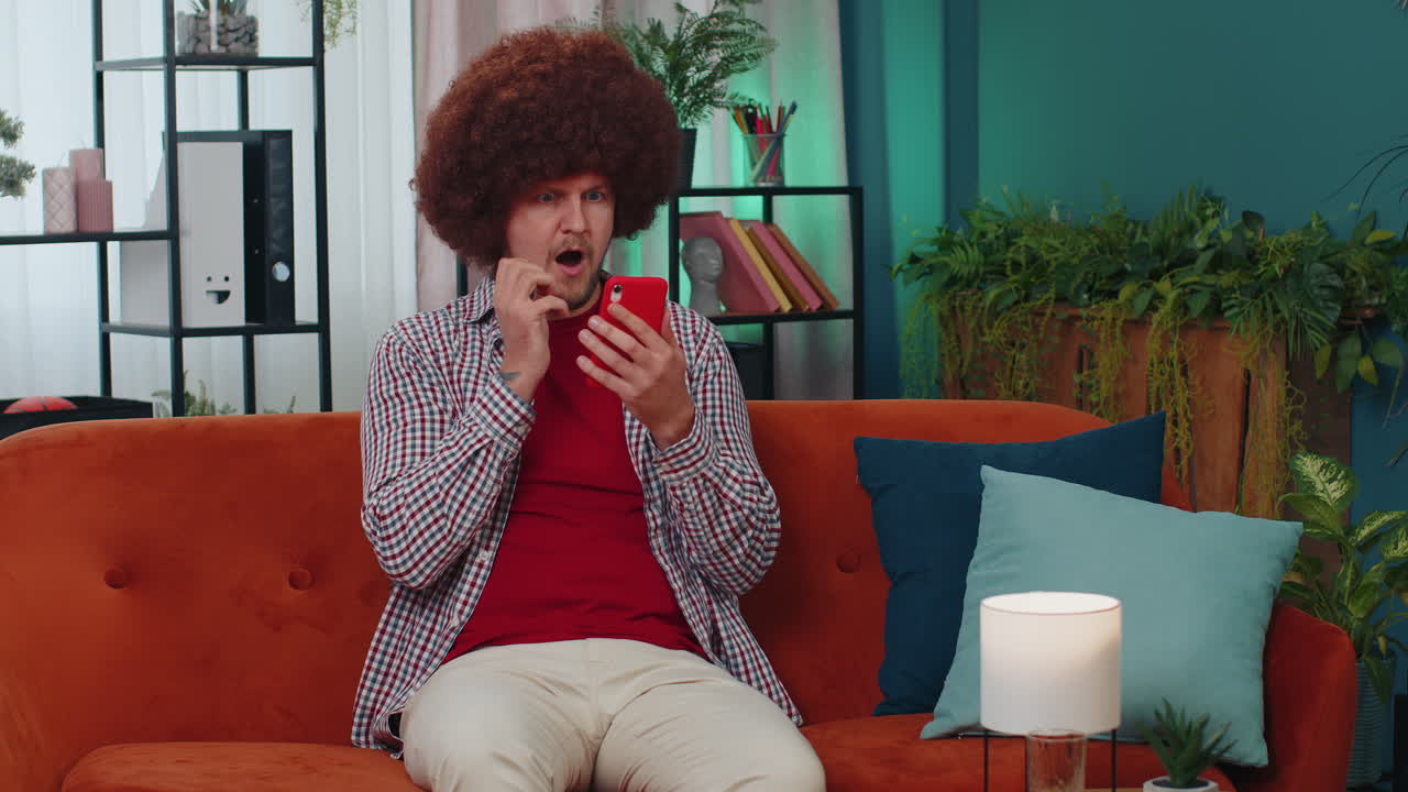 Flot ung mand derhjemme bruger smartphone til at taste og browse, wow, ja, opdagede en stor gevinst og fejrer!