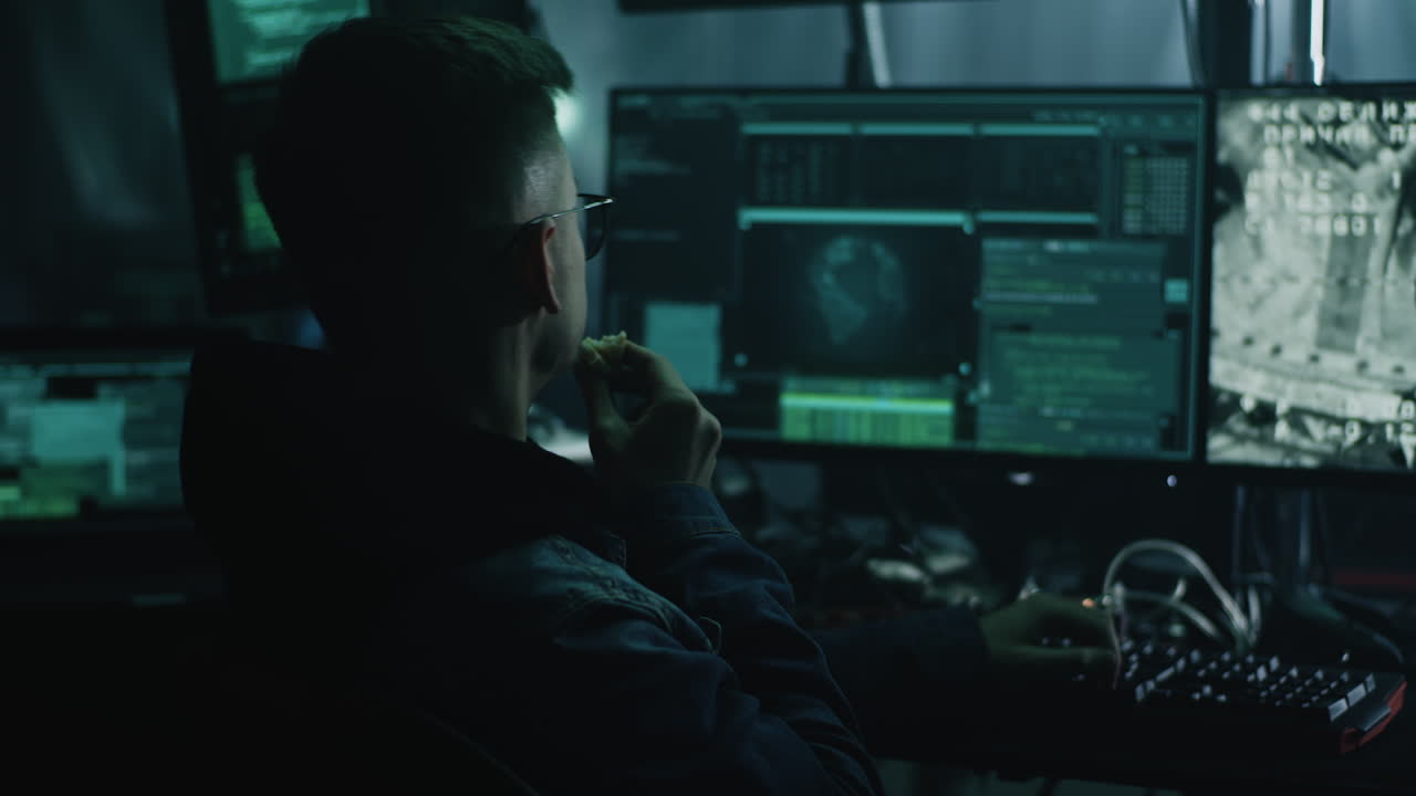 Hacker working on multiple computers in a dark room