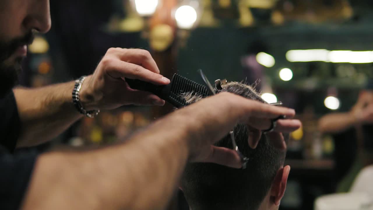 Slow Motion shot: Close Up view of the barber's hands performing a haircut with scissors and combing the client