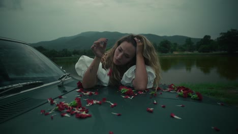 woman with flowers on a vintage car near a lake