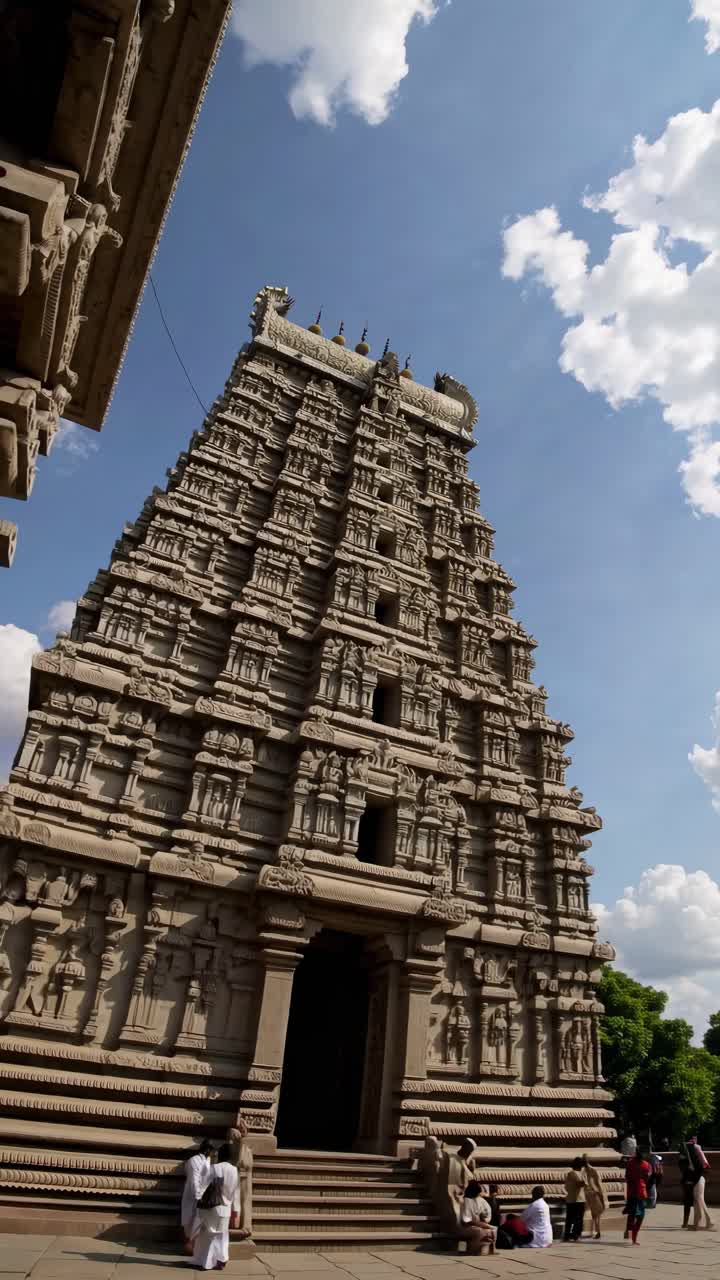 A low-angle video shot of a majestic temple tower against a vibrant blue sky with fluffy clouds
