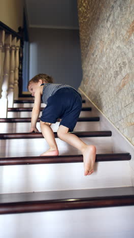 following a toddler boy crawling up the stairs on all four. cute toddler boy turns around and sits on the stair. vertical video.
