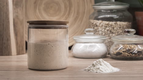 sourdough starter yeast rising in a glass jar with heap of flour on the side - fermentation - zoom-in shot, time lapse