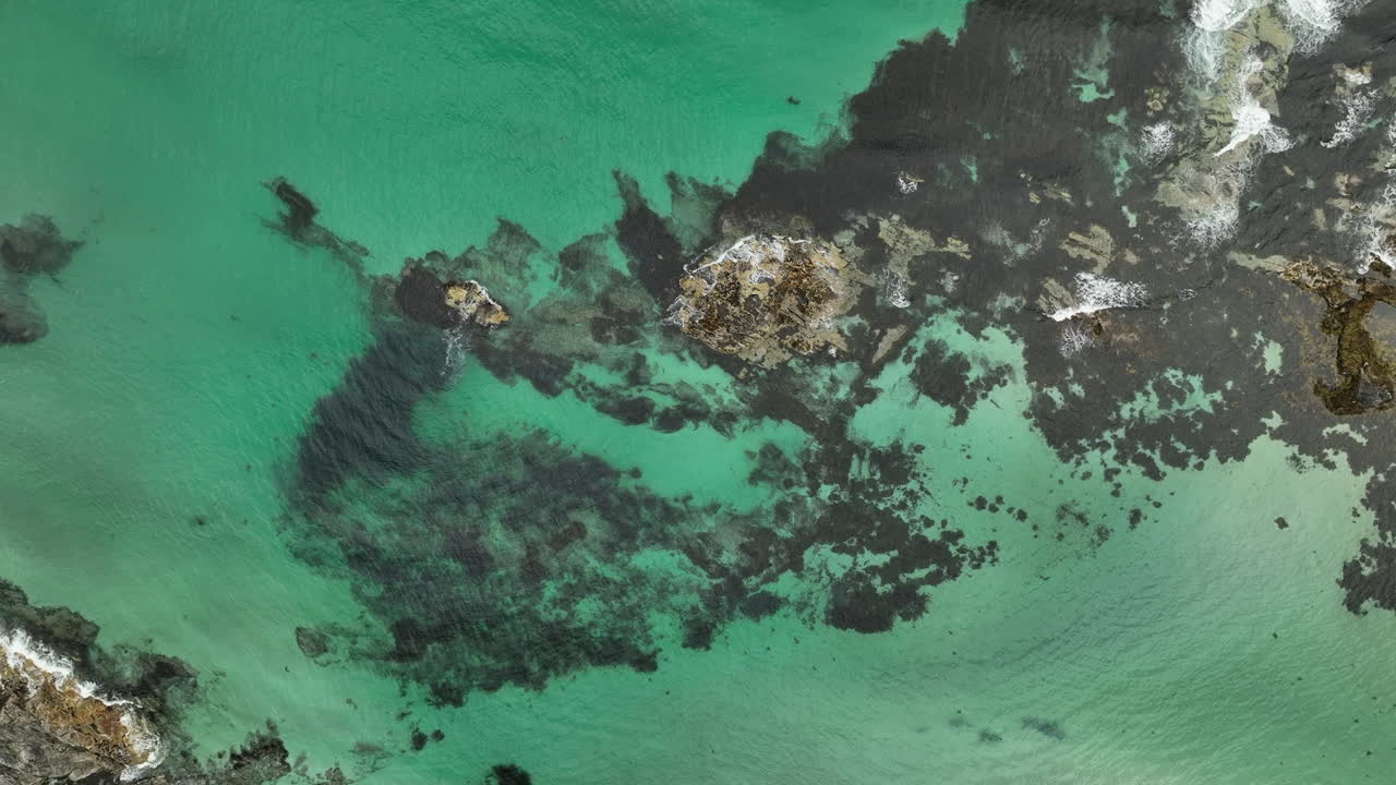 Spiral aerial view showing sand underwater and waves crashing on rocks in Lofoten, Norway