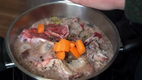 fresh orange carrots added to bone broth pan, in close-up slow motion