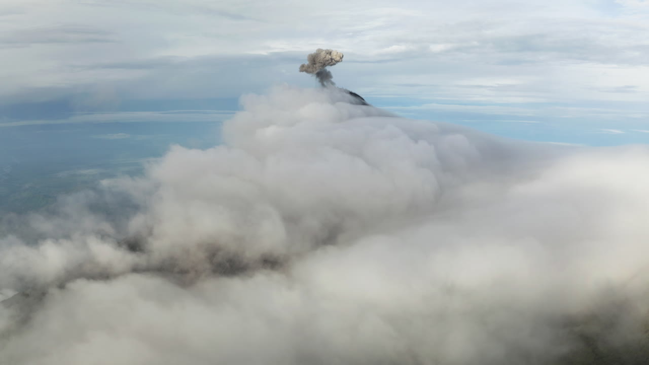 어두운 회색의 검은 연기가 구름 속에 가려진 화산 위로 올라와 굴러갑니다. - 과테말라