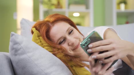 beautiful woman lying down at home texting on her phone thoughtfully and happily.