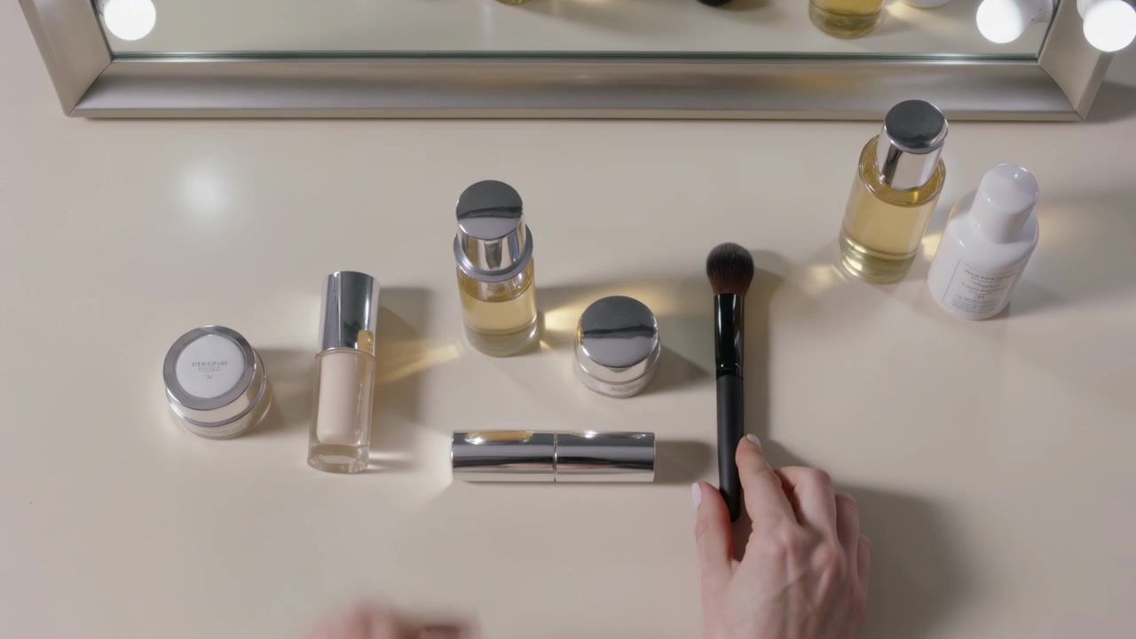 Entering frame, cream sweater hands lifting pumps, turning caps, placing brush on vanity prepping