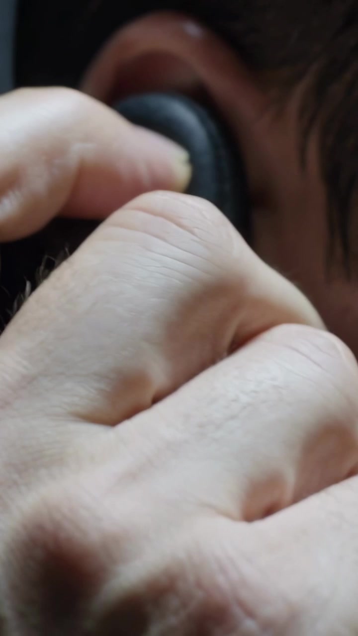 Vertical video: Bringing adult hand pressing padded cup to ear in close-up, adjusting fit