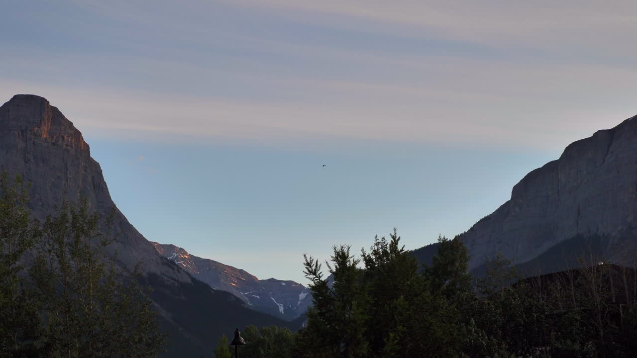 캐나다 로키 산맥, 앨버타, 캐나다의 산봉우리 사이에 있는 계곡 위로 행글라이딩하는 사람