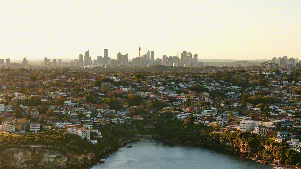 Coastline of Clovelly and distant Sydney city skyline under hazy afternoon light, aerial establishing orbit