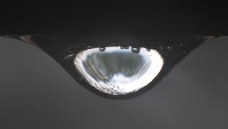 close-up of vibrant rainwater droplet, particles moving within shiny surface