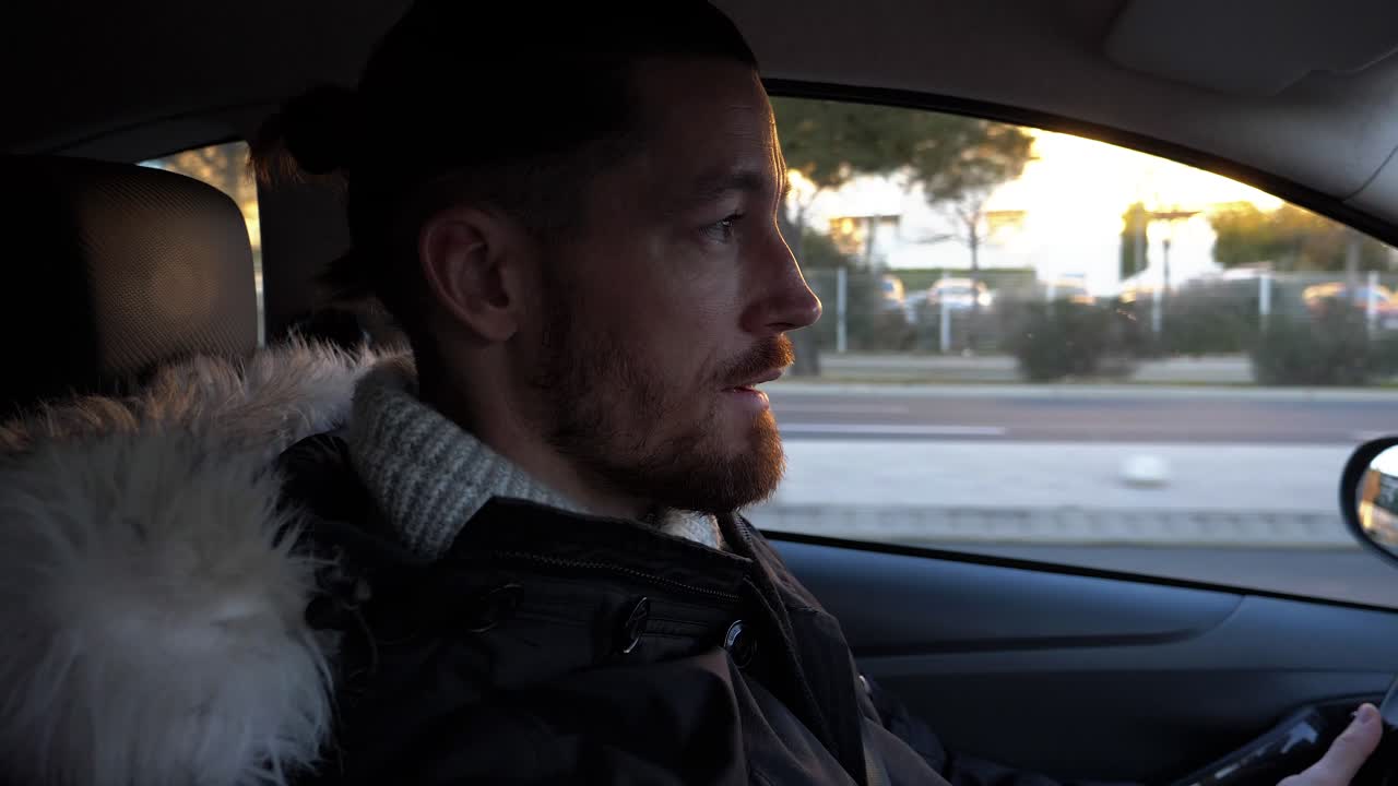 En mand taler i sin bil; han har sin frakke på.