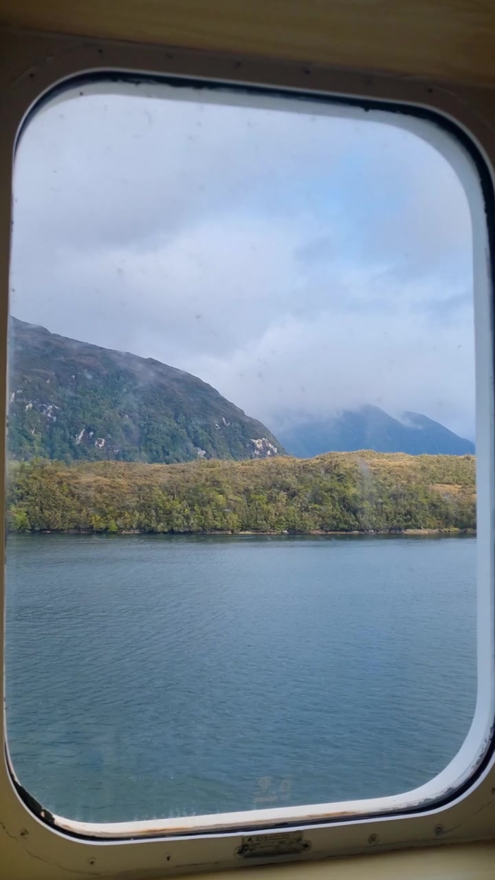 View through a ferry window of Chilean Patagonia, featuring calm fjord waters, forested mountains, and pristine wilderness. Scenic ferry journey through one of South America's most spectacular natural