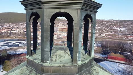 City-view-seen-trough-gaps-in-top-of-Kongsberg-church-tower-Norway---Background-landscape-passing-fast-while-drone-rotating-with-church-in-closeup-foreground