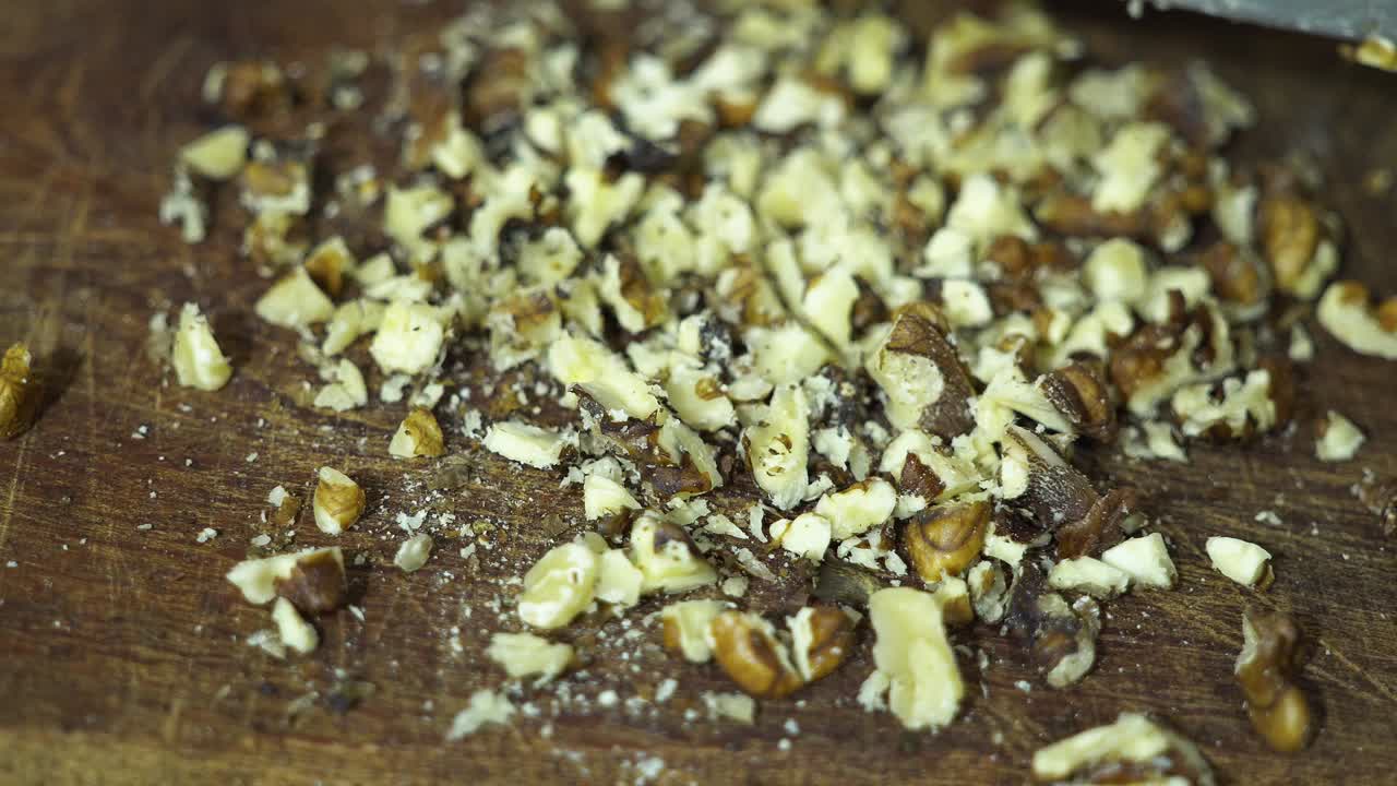 Closeup of a person's hand using a knife to chop nuts on a wooden table.