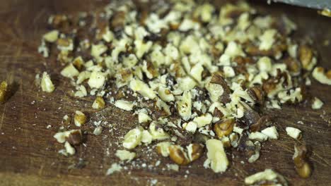 closeup of a person's hand using a knife to chop nuts on a wooden table.