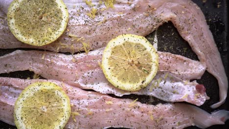 filete de merluza fresca en una bandeja para hornear con rodajas de limón, sazonada con pimienta negra molida y hierbas