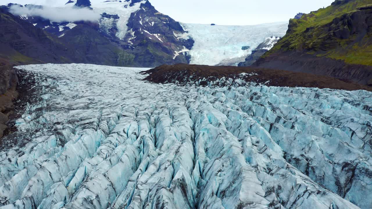 drone volando sobre el glaciar svinafellsjokull con profundas grietas en el hielo azulado con vetas de ceniza negra en islandia