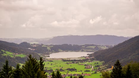 this timelapse video captures the tranquil alpsee nestled in the hills of allgäu, bavaria, germany. sailboats drift across the water, surrounded by rolling pastures and forests beneath a cloudy sky.