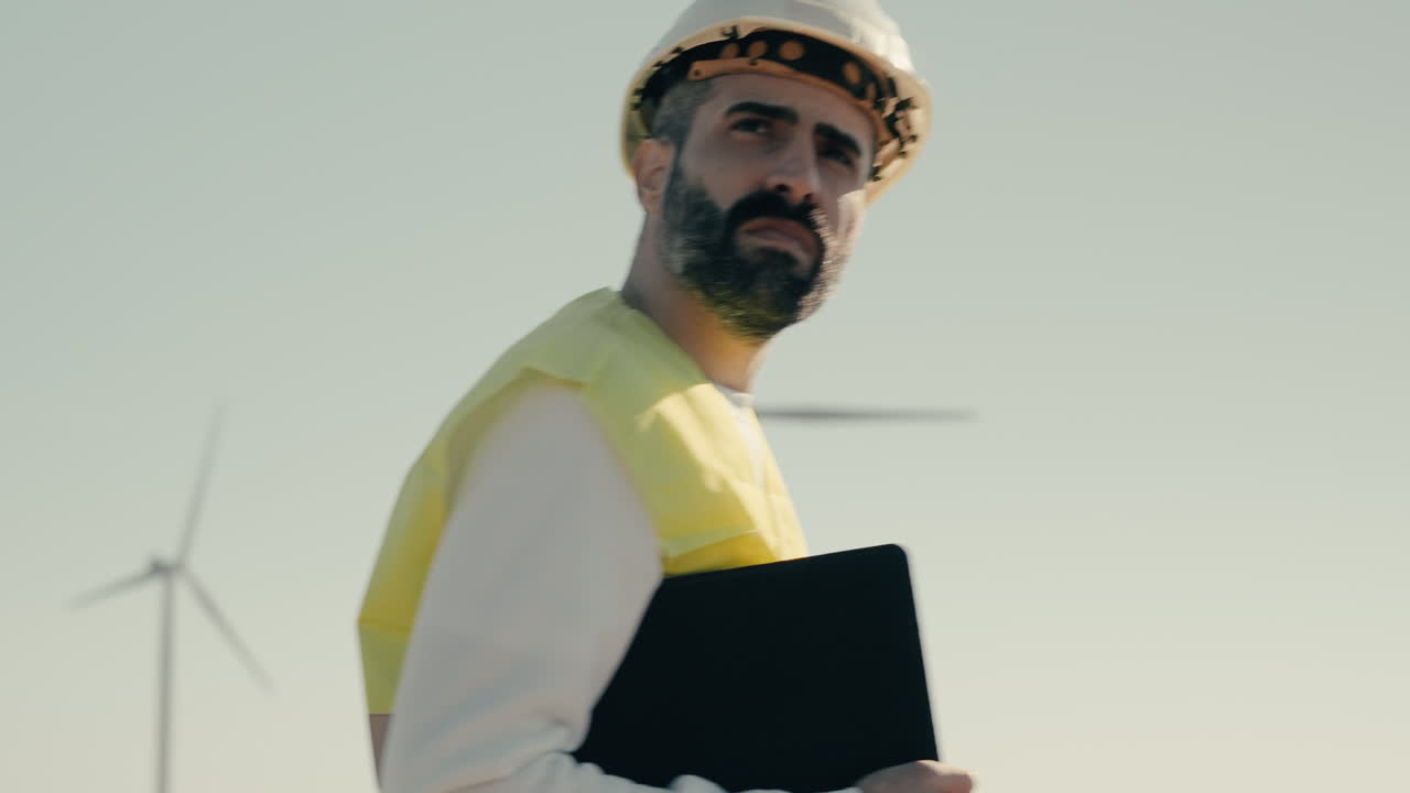 An experienced engineer in a reflective vest checks wind turbines on a sunny day, representing the future of clean energy and sustainability