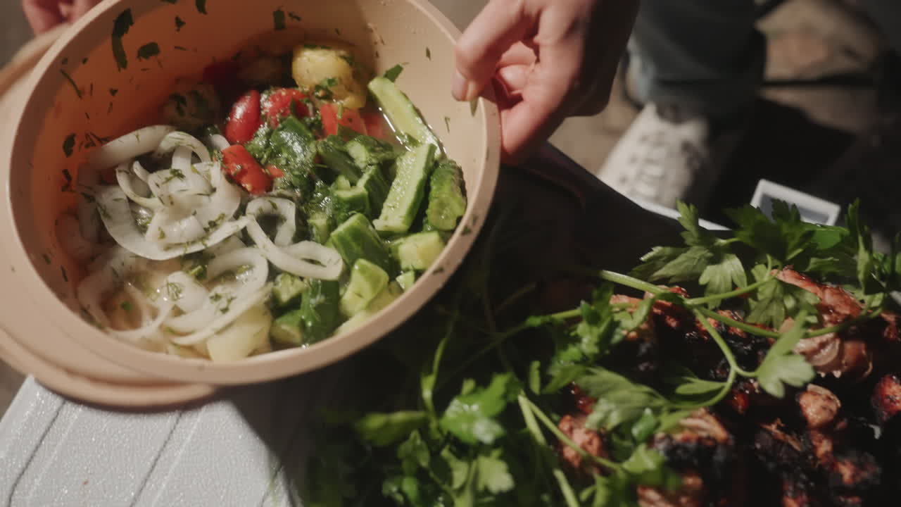 Fresh camping salad bowl with avocado, camper lifts lid to reveal mixed salad of avocado, onion, tomato and herbs, mixing bowl and platter of grilled chicken beside, vibrant greens and sunlight create