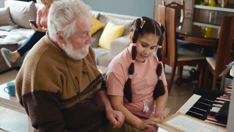 el abuelo y la nieta tocan el piano en casa. la niña con un anciano se está divirtiendo tocando el piano. la familia feliz canta y juega.