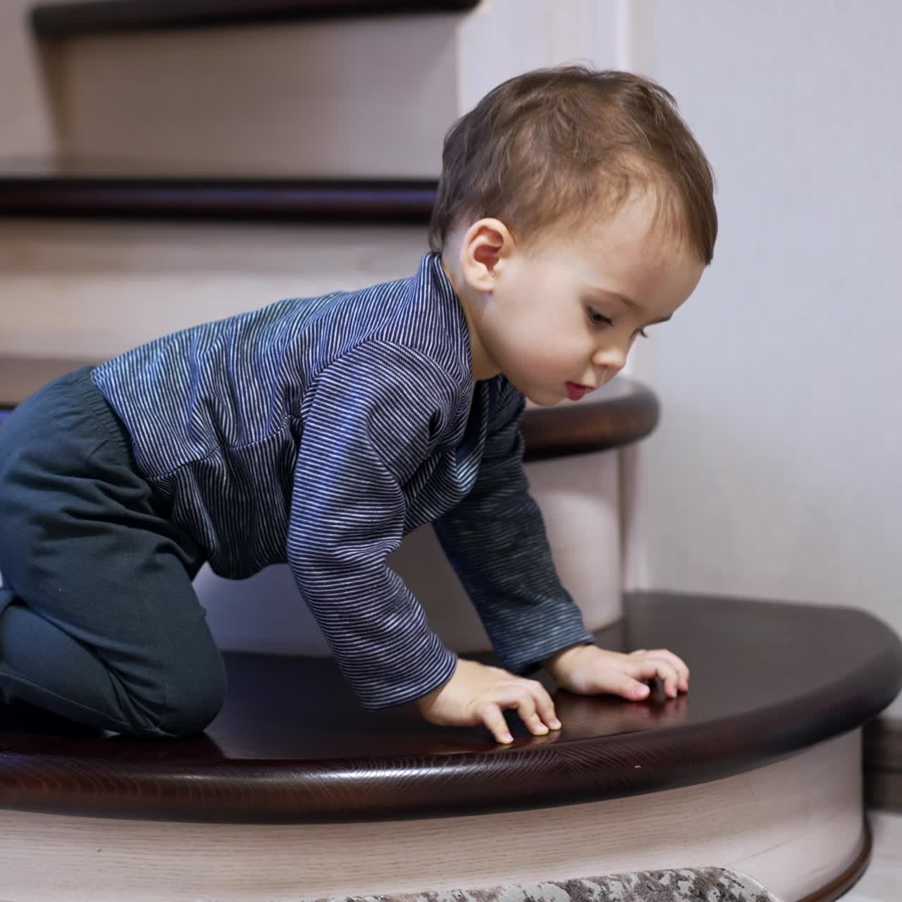 Caucasian baby boy standing on all four on the stair. Cute kid plays with a toy dropping it on the floor