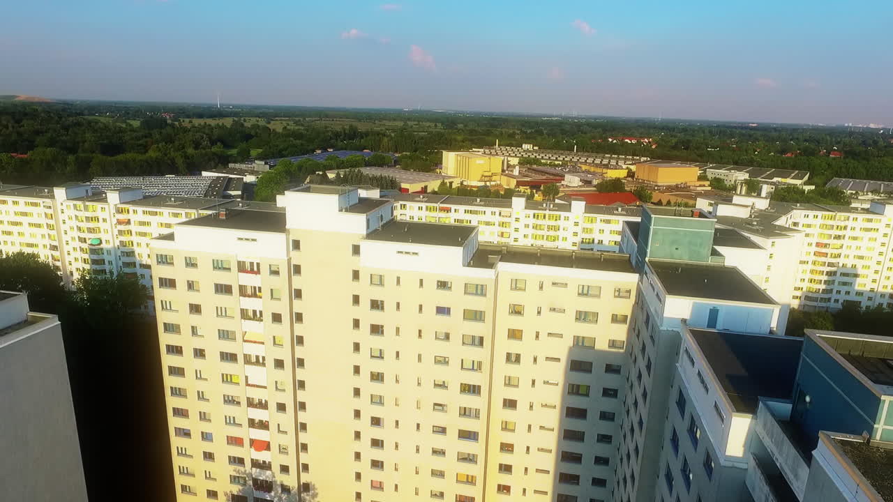 Drone naik di atas bangunan tempat tinggal berwarna putih, menampakkan blok perkotaan padat di belakangnya
