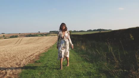 young woman in a long dress walks through a field and spins