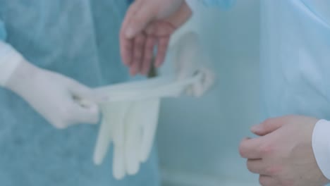 nurse assisting surgeon and helping with gloves in operating room at hospital