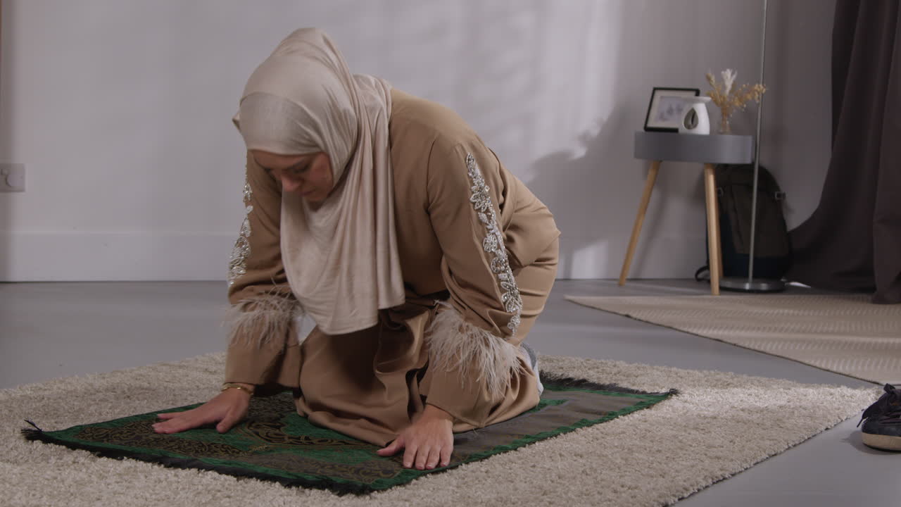 헤자브를 입은 무슬림 여성이 집에서 기도할 때 기도 매트 7에 무을 고 기도합니다.