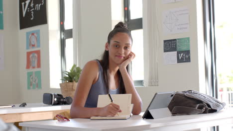 in high school, teenage girl writing in notepad and using tablet in classroom