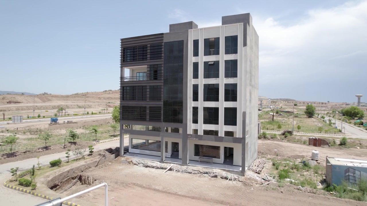 Um edifício moderno de vários andares ergue-se entre estradas e terrenos não urbanizados num canteiro de obras ativo.