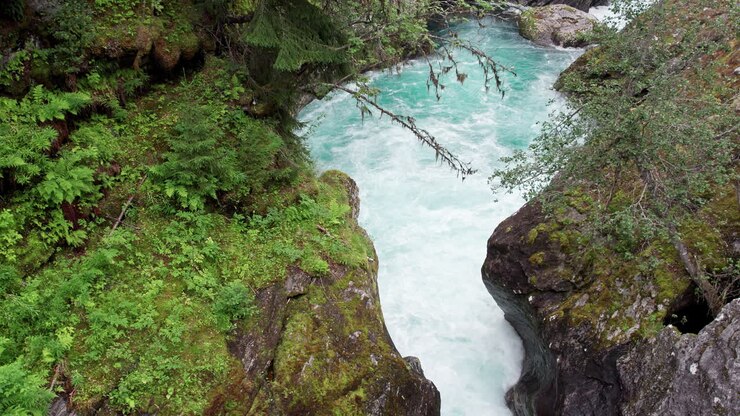 Crane shot, camera climbing from white water rushing between two moss covered rocks