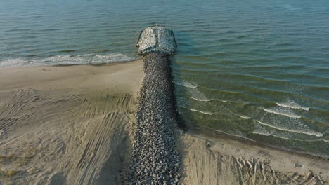 aerial birdseye view of protective stone pier with concrete blocks and rocks at baltic sea coastline at liepaja, latvia, strengthening beach against coastal erosion, drone shot moving forward