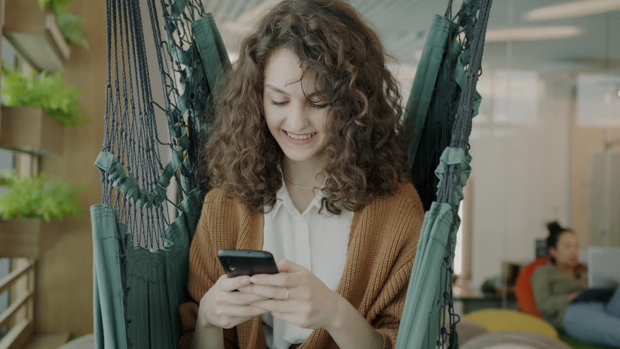 Woman using a smartphone in a hammock in a modern office