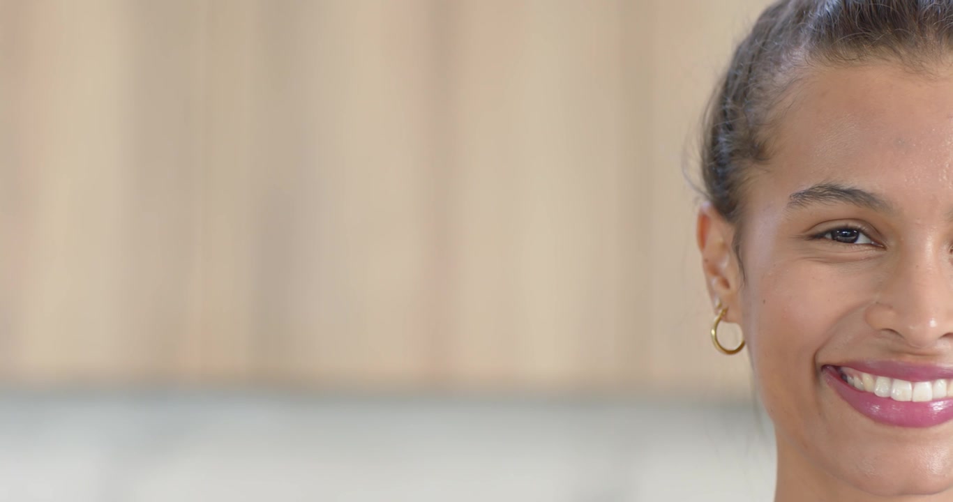 Donna afroamericana con orecchini a cerchio d'oro e chignon, che reagisce a un segnale, sorridendo e posando in cucina, con spazio per il testo.