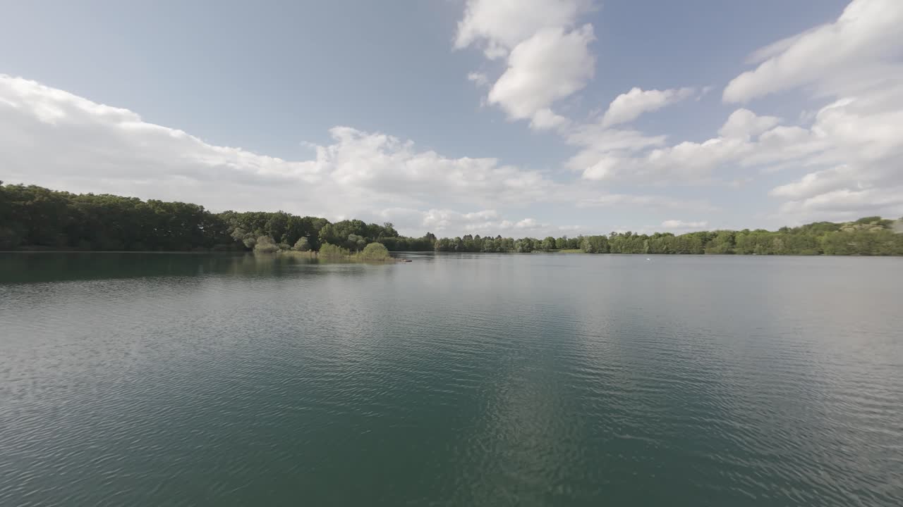 Aerial water view of a calm lake, a green forest in the back and a cloudy sky