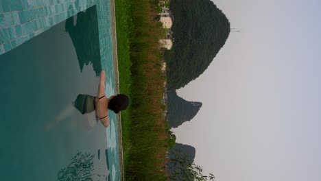 woman bathing in pool at sunset with karst mountain views in yangshuo, china. vertical screen