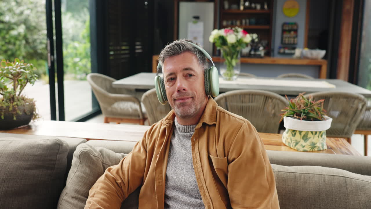 Mann som slapper av i sofaen hjemme mens han lytter til musikk med hodetelefoner