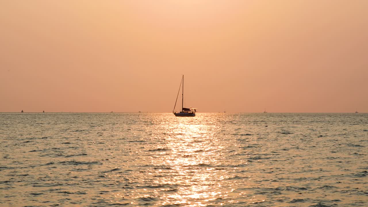 A Yacht with Sunset Reflection in the Center of Frame on the Horizon in the Distance. Stationary Medium Zoomed Shot in 4K