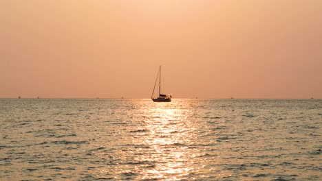 a yacht with sunset reflection in the center of frame on the horizon in the distance. stationary medium zoomed shot in 4k