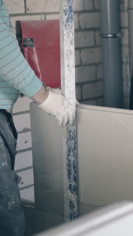 professional painter in white gloves measures gypsum plasterboard height holding long special ruler close view