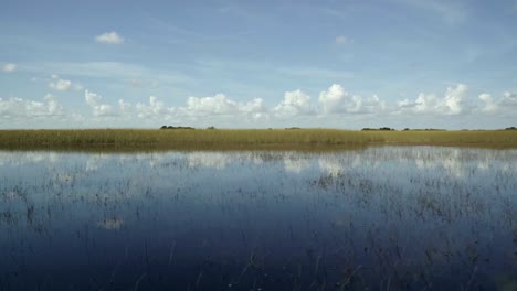 rápido camión a la izquierda de la impresionante florida everglades cerca de miami montando en un airboat con el agua del pantano tranquilo reflejando el cielo y creando un espejismo rodeado de hierba alta en un día soleado